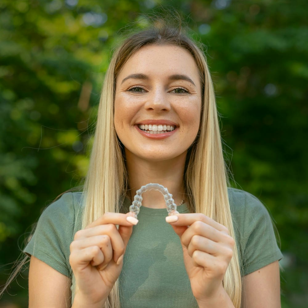 Smiling young blonde woman holding Invisalign with two hands