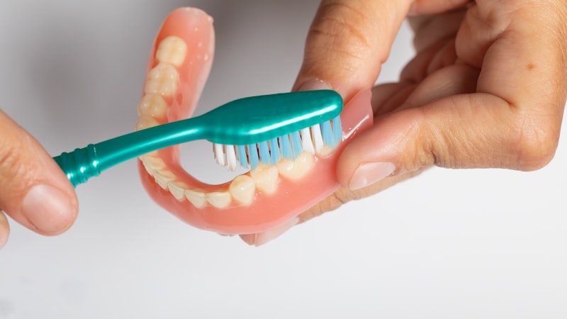 hands holding and brushing dentures